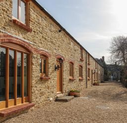 A stone building with wooden windows and doors along a gravel pathway at The Granary Burton Bradstock