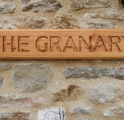 A wooden sign with the words THE GRANARY carved into it mounted on a stone wall at The Granary Burton Bradstock