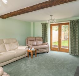 A living room with leather sofas wooden tables and glass doors leading outside at The Granary Burton Bradstock