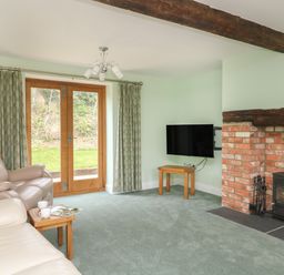 A living room with a fireplace a mounted television leather sofas and wooden doors at The Granary Burton Bradstock