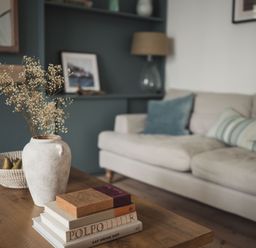 A living room with a wooden coffee table holding a vase with flowers and stacked books at Fairhaven in Dartmouth