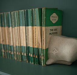 A row of vintage green penguin books supported by a whale-shaped bookend on a green shelf at Fairhaven in Dartmouth