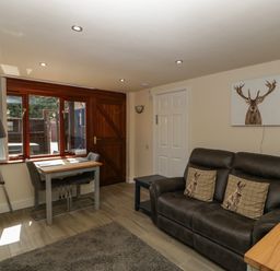 A living room with a dark sofa and animal cushions a small dining table with two chairs and a tripod lamp at The Retreat in Washford near Williton
