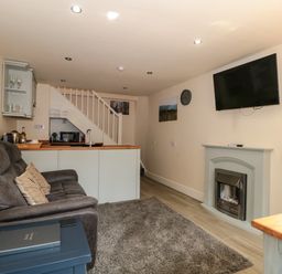A living area with a brown sofa and pillows a fireplace and a mounted television at The Retreat in Washford near Williton