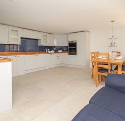 A kitchen with white cabinets wooden countertops blue backsplash and a dining table with wooden chairs at The Stables Burton Bradstock