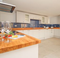 A kitchen with wooden countertops white cabinets a bottle of wine two wine glasses and vegetables on the counter at The Stables Burton Bradstock