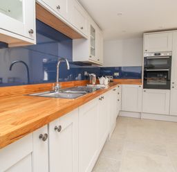 A kitchen with white cabinets wooden countertop blue backsplash and a double oven at The Stables Burton Bradstock
