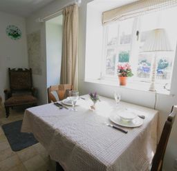 A dining area with a table set for two near a window with a lamp and flowers at Noel Cottage in Chipping Campden