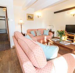 A living room with two pink sofas and a wooden coffee table with flowers and magazines at Cowfair Cottage in Chipping Campden