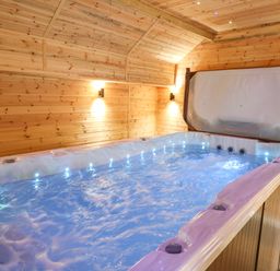 An indoor room with wooden walls and ceiling featuring a large hot tub with water and lights at Tynewydd Fields in Cross Inn