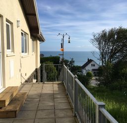 A patio with steps and a railing next to a house with a view of the sea and trees at Aelwyd Y Don in Tresaith