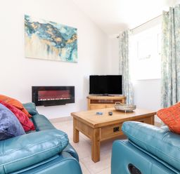 A living room with teal sofas orange and purple cushions a wooden coffee table a wall-mounted electric fireplace and a television at Chy-Whel in Sticker