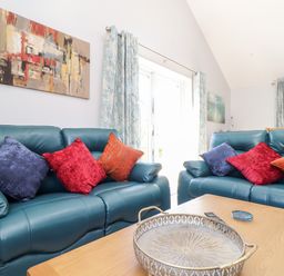 A living room with teal leather sofas with colorful cushions and a wooden coffee table with a decorative tray and coasters at Chy-Whel in Sticker