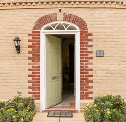 The front entrance of a brick house with a partially open pale green door and yellow flowers by the path at Coral House in Overstrand