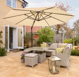 An outdoor patio area with wicker furniture and cushions under a large umbrella at Coral House in Overstrand