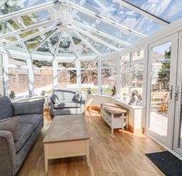 A conservatory with glass roof and windows containing grey sofas a wooden coffee table and side table at Harbour Lights in Torquay