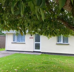A small house with two windows and a door surrounded by grass and a tree at Lands End in Liskeard near St Cleer