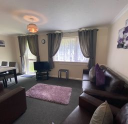 A living room with two brown sofas, a small table with a TV, grey curtains on windows, and a dining table with chairs at Lands End in Liskeard near St Cleer
