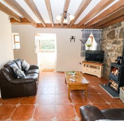 A living room with a leather sofa coffee table wood burning stove and television at Bwthyn Siop Pencaerau Rhiw near Aberdaron