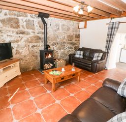 A living room with brown sofas a wood burning stove and a wooden coffee table at Bwthyn Siop Pencaerau in Rhiw near Aberdaron