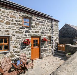 Stone cottage exterior with wooden door two wooden chairs and hanging flower baskets at Bwthyn Siop Pencaerau in Rhiw near Aberdaron