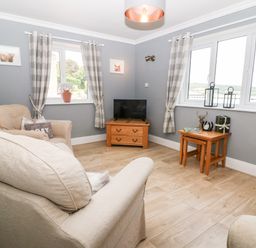 A sitting room with armchairs a television on a wooden stand and plaid curtains at Farm View Lodge in Painswick