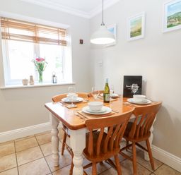 A dining area with a wooden table set for four under a hanging light at Farm View Lodge in Painswick