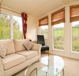 A living room with beige sofas a glass coffee table and a black chair near windows with wooden blinds at Exe Valley Lodge in Bampton Devon