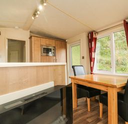 A dining area with a wooden table and black chairs next to a window with red curtains in a kitchen space at Exe Valley Lodge in Bampton Devon