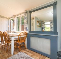 A dining area with a wooden table and four chairs near windows with floral curtains at Valley Lodge in Bampton Devon