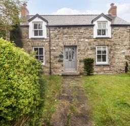 Stone cottage with gray door and four windows surrounded by grass and bushes at Sea View in Newport Pembrokeshire