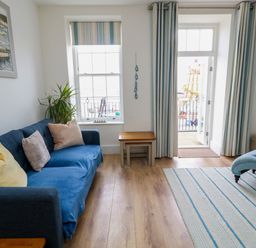 A living room with a sofa and window leading to a balcony at 4 The Beaches in Weymouth