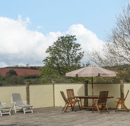An outdoor patio area with loungers and a table with chairs under an umbrella at The Pool House in Crediton