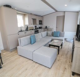 A living room with a gray sectional sofa and a small coffee table next to a kitchen with beige cabinets and appliances at Dreams & Streams in Bockenfield Country Park near West Thirston