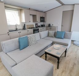 An open plan kitchen and living room with a gray sectional sofa and small coffee table at Dreams & Streams Bockenfield Country Park near West Thirston