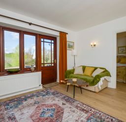 A living room with a sofa green throw wooden coffee table and large windows at Little Barton in Stogumber near Watchet