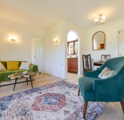 A living room with green sofa, wooden coffee table, blue armchair, dining table, and kitchen visible through an arch at Little Barton Stogumber near Watchet