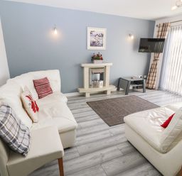 A living room with white sofas a small fireplace a wall mounted tv and vertical blinds at Beach Reach in Valley