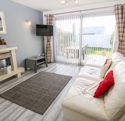 A living room with a white sofa with cushions a gray rug a fireplace a wall mounted tv and sliding glass doors with vertical blinds at Beach Reach in Valley
