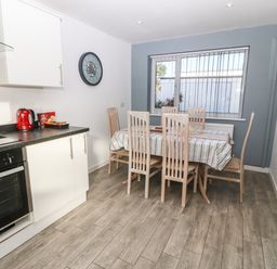 A dining area with a table and six chairs next to a kitchen with white cabinets and a red kettle at Beach Reach in Valley