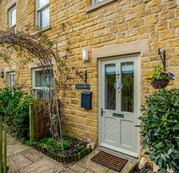 The exterior door of a stone cottage with plants a wooden fence and hanging flower baskets at Jasmine Cottage in Mickleton Gloucestershire
