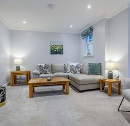 A living room with a leather corner sofa wooden tables lamps and artwork at Jasmine Cottage in Mickleton Gloucestershire