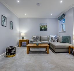 A living room with a grey sofa wooden coffee and side tables lamps and framed pictures on walls at Jasmine Cottage Mickleton Gloucestershire