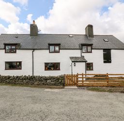 A white farmhouse with a slate roof a stone wall and a wooden gate at Orsedd Wen Farmhouse in Betws-Y-Coed