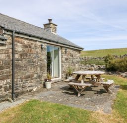 A stone cottage with a wooden picnic table on a stone patio in a grassy yard at Orsedd Wen Cottage in Betws-Y-Coed