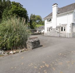 An outdoor view of a house with a stone wall and grass at Pengwern Bach Llanrwst