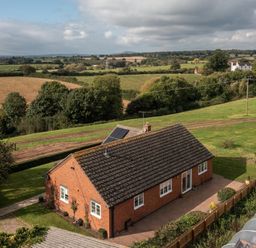 A red brick single-story house with a tiled roof and solar panels in a rural setting at Overbrook in Salwarpe near Droitwich Spa