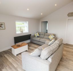 A living room with two grey sofas a wooden coffee table a model sailboat on a window sill and a framed turtle picture on the wall at Caban Y Mor in Amroth near Saundersfoot