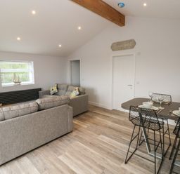 A living room with two gray sofas and a dining table set for four at Caban Y Mor in Amroth near Saundersfoot