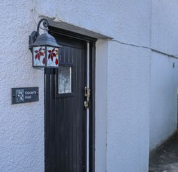 A black wooden door with a decorative stained glass lantern and a sign that reads Oscars Pad on a textured white wall at Oscars Pad in Brynsiencyn